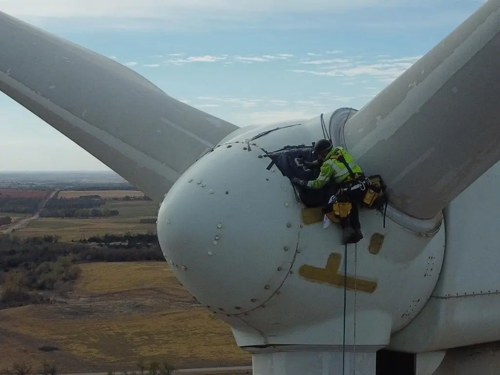 Technician on rope at the hub of a wind turbine, working on the nose cone