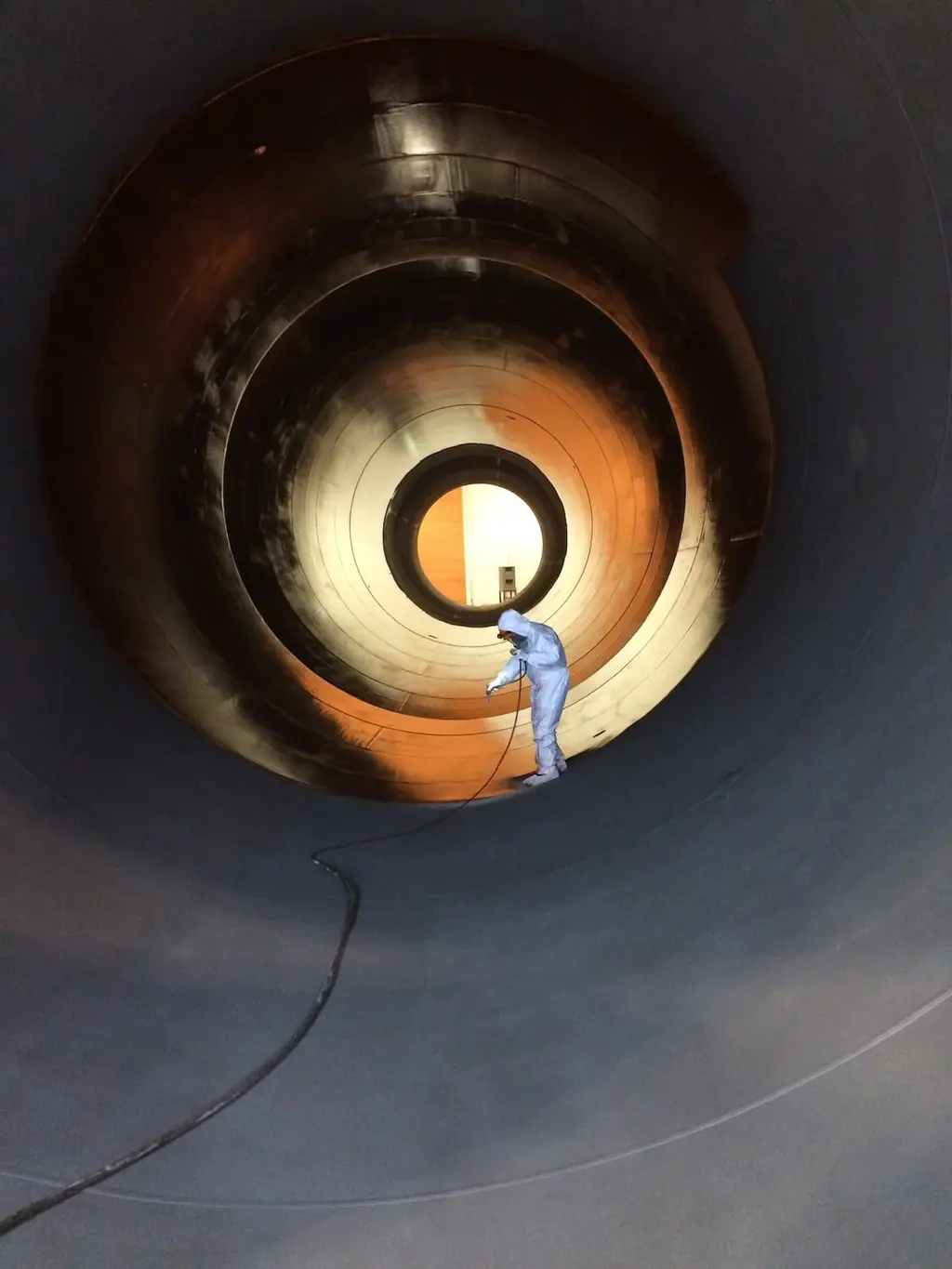 Technician in a white protective suit spray-coating the inside of a wind turbine tower